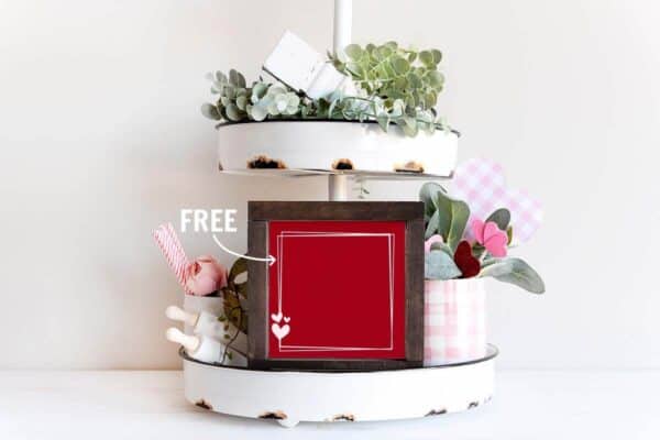 Horizontal image of a tiered tray with Valentine decorations and red frame with free heart SVG in white vinyl.