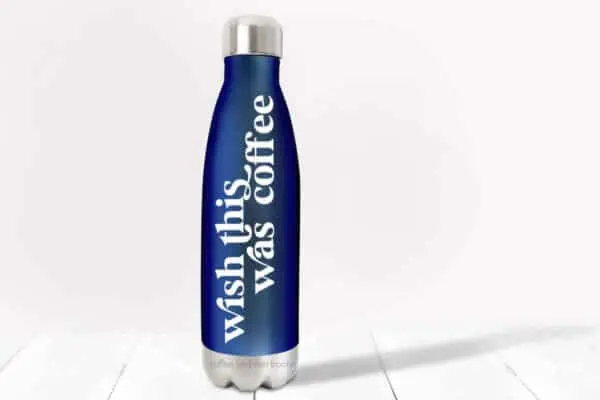 Blue water bottle with white vinyl which reads wish this was coffee on wood with light pink background.
