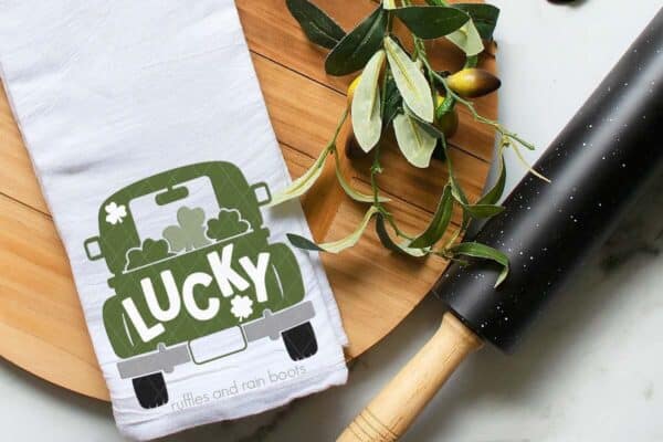 Horizontal image of a white kitchen towel with green lucky truck SVG for St Patrick's Day with shamrocks on wood cutting board.
