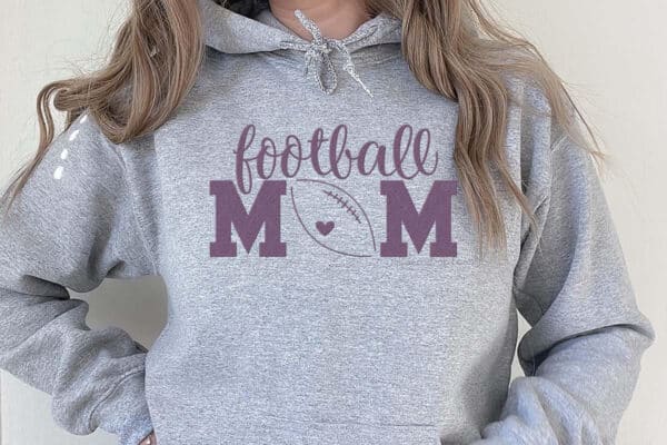 Horizontal image of woman in gray sweatshirt with lavender vinyl football mom SVG cut out and pressed.