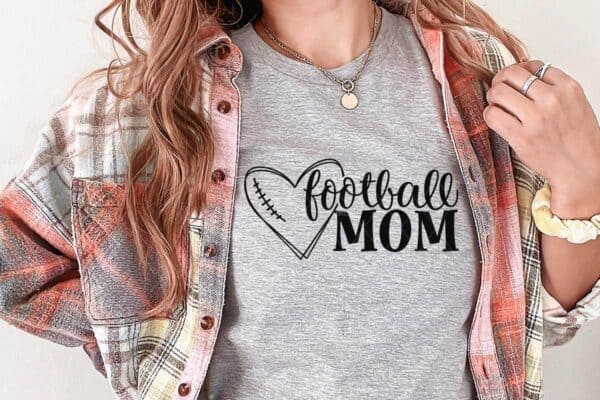 Horizontal image of woman in flannel and gray t-shirt with football mom in black vinyl with football heart SVG.