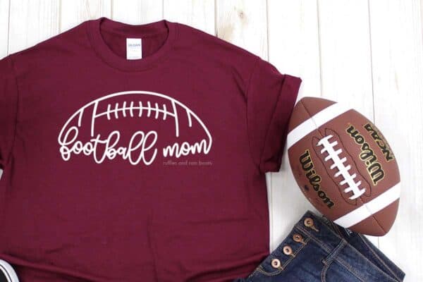 Football mom design cut from white vinyl pressed onto maroon t-shirt with football background.
