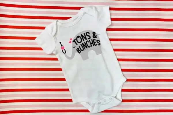Horizontal image of baby body suit on striped background with I love you tons and bunches in vinyl.