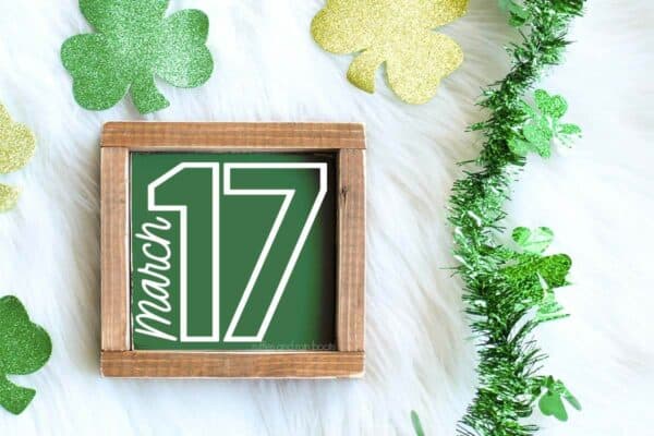 Horizontal image of green wood sign with white March 17 in white vinyl on festive St Patrick's Day background.