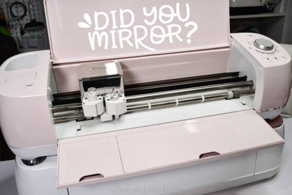 Horizontal image of pink Cricut machine stacked on craft table with white vinyl that says Did you Mirror?