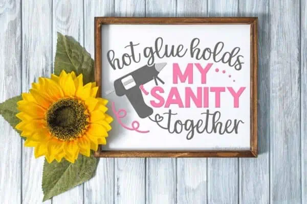 Horizontal image of a white sign with hot glue holds my sanity together in pink and gray vinyl next to a sunflower.