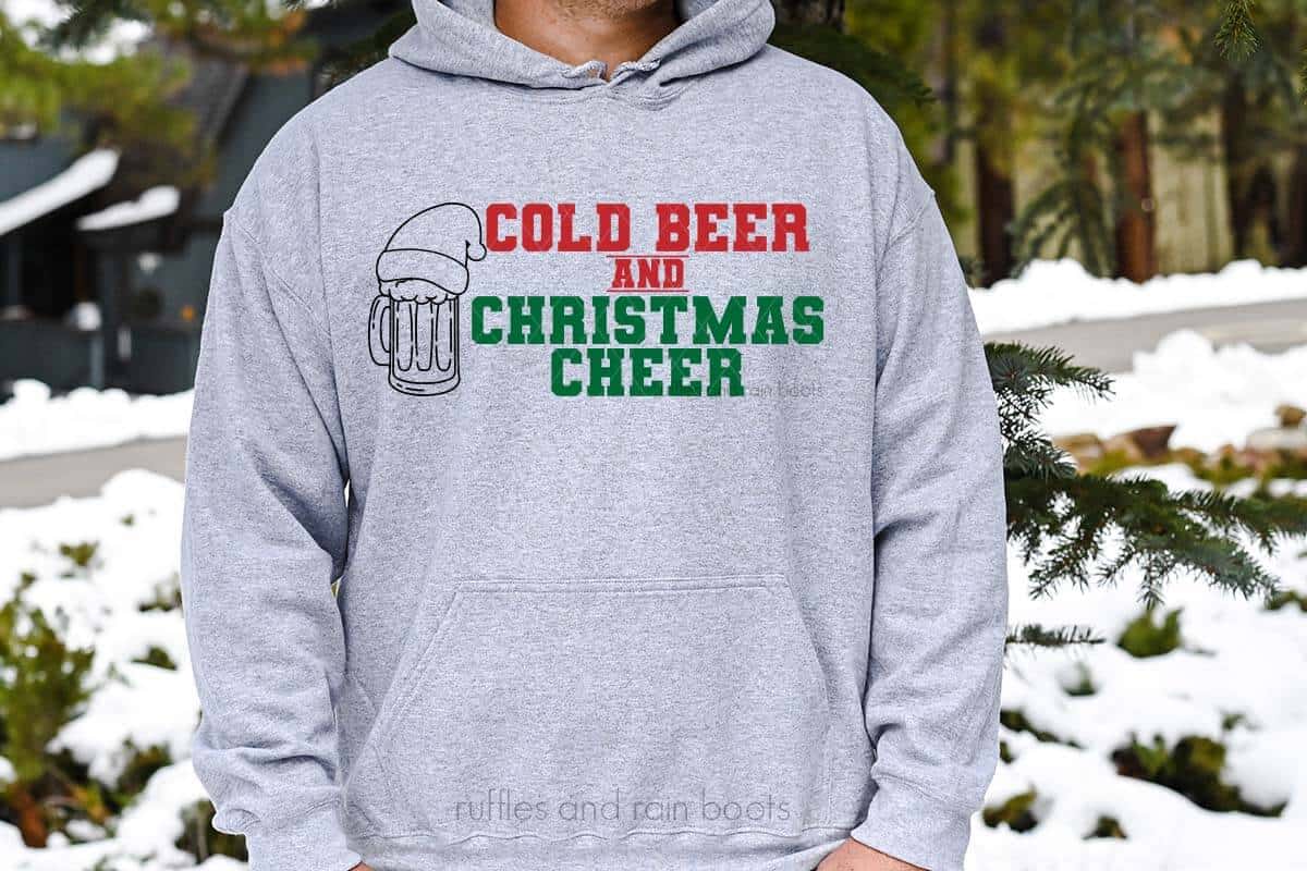 Horizontal image of man wearing heather gray sweatshirt which reads cold beer and Christmas cheer with beer stein in a Santa hat.