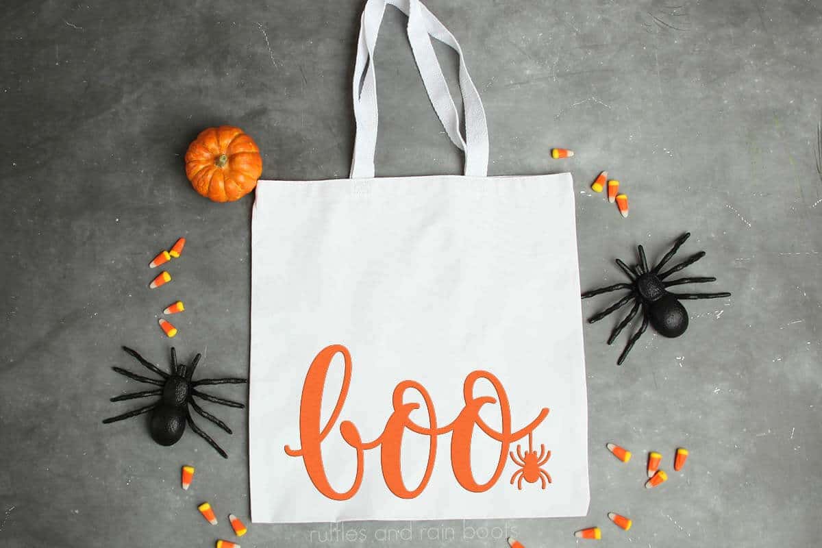 Horizontal image of a cotton tote on gray concrete which reads boo in orange vinyl with spider SVG.