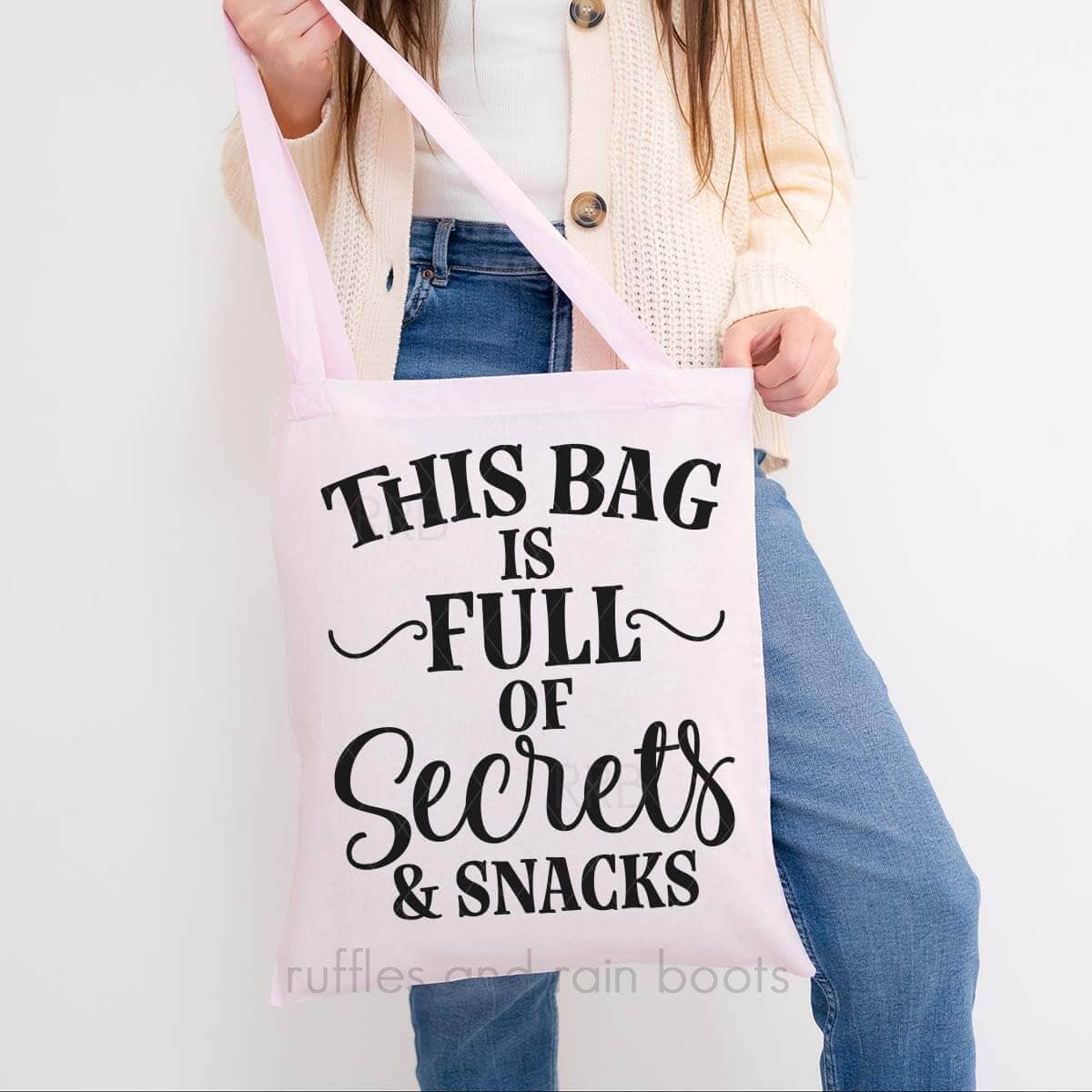 Woman in jeans holding pink tote bag which reads this bag is full of secrets and snacks.