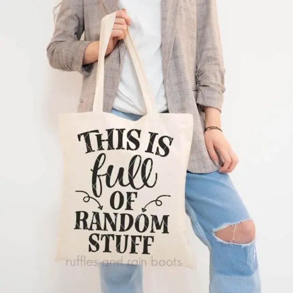 Vertical image of woman in blazer and jeans holding canvas tote which reads this is full of random stuff.