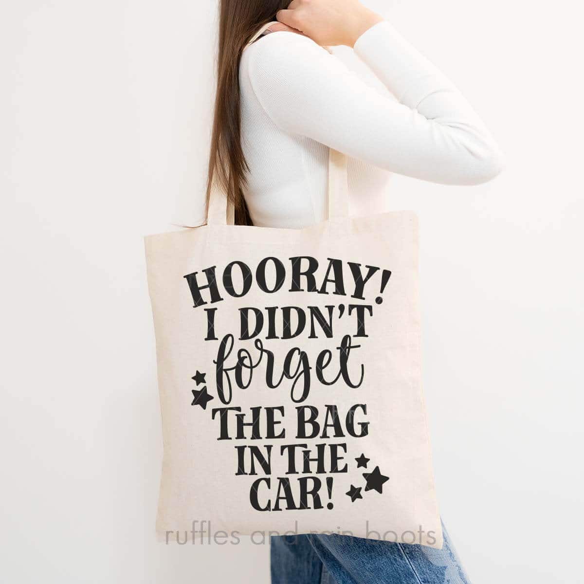 Vertical image of woman in white t-shirt holding tote bag which reads hooray I didn't forget the bag in the car.