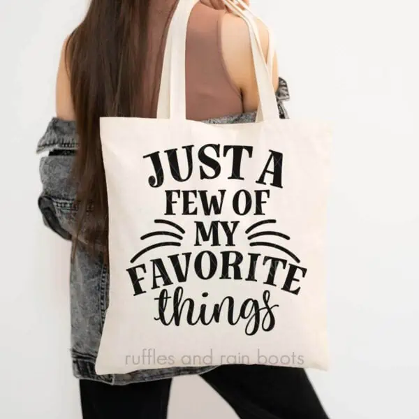 Vertical image of woman holding a natural tote bag which reads just a few of my favorite thing from Ruffles and Rain Boots.