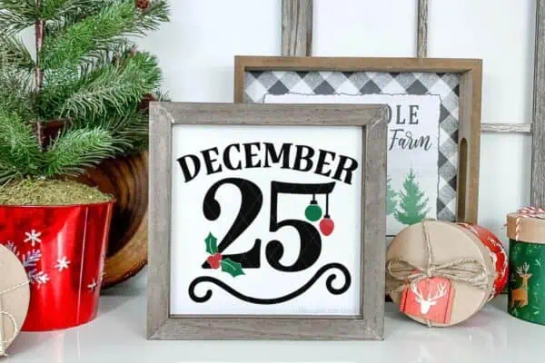 Horizontal image of December 25th SVG placed in permanent vinyl on square sign in front of a holiday background.