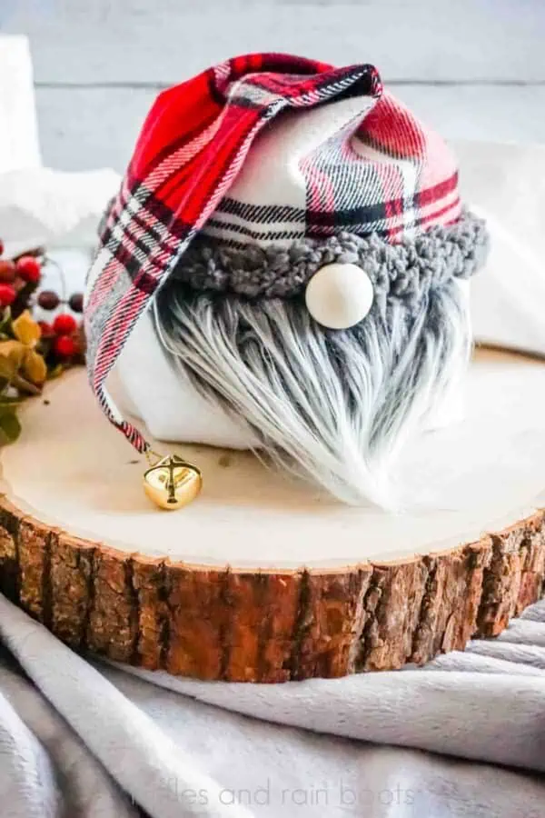 Vertical image of Christmas gnome in red and black flannel hat and gray beard on a wood round with berries and toilet paper rolls.