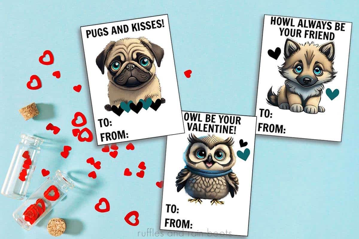 Horizontal image of blue table with red paper hearts and three Valentine printable cards with animals: a pug, an owl, and a wolf.