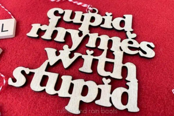 Horizontal image of a laser cut wood ornament which reads cupid rhymes with stupid on a red background.
