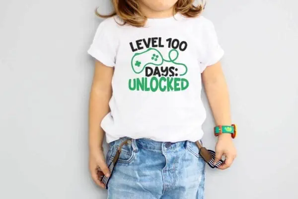 Horizontal image of a little boy in a white t-shirt which reads level 100 days unlocked.