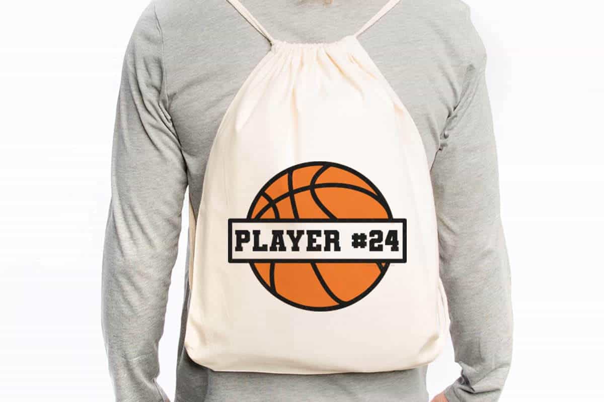 Horizontal image of a man in a light gray long sleeve shirt with a drawstring backpack with a basketball in orange and black.