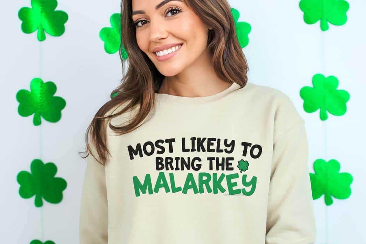 Horizontal image of a white background with shamrock banner and a woman in a tan sweatshirt with most likely to bring the malarkey in black and green.