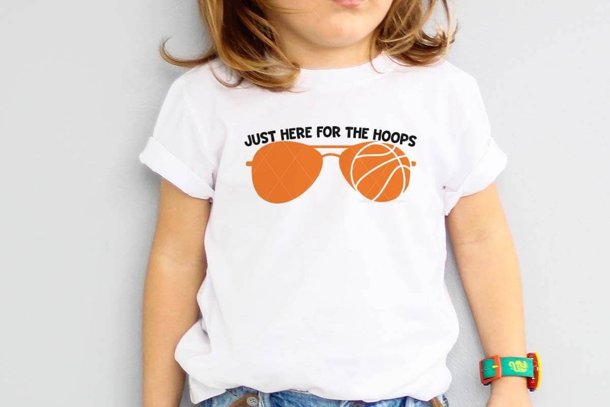 Horizontal image of a little boy wearing a white t-shirt which reads just here for the hoops in black lettering with orange basketball sunglasses.