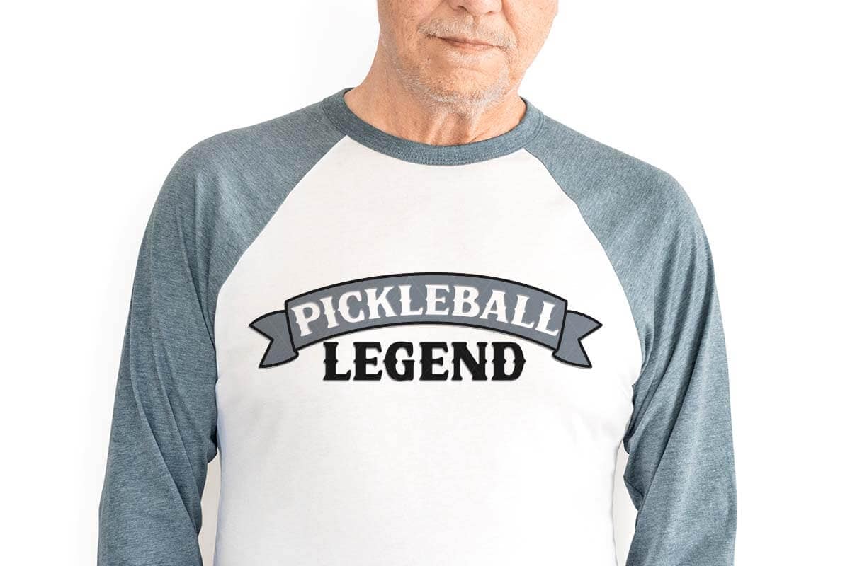 Horizontal image of an older man in a raglan shirt with pickleball legend in black and blue vinyl.