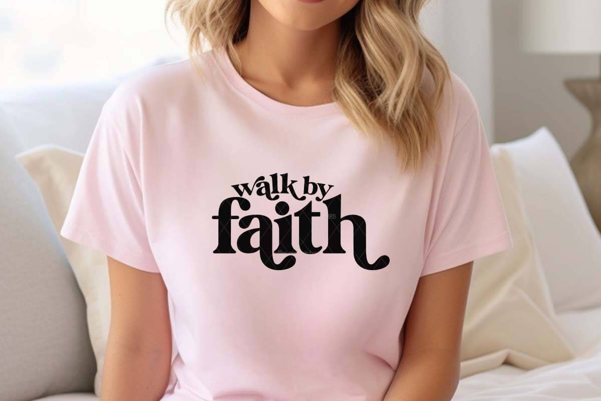 Horizontal image of woman on couch in pink shirt which reads walk by faith made with SVG and Cricut black heat transfer vinyl.