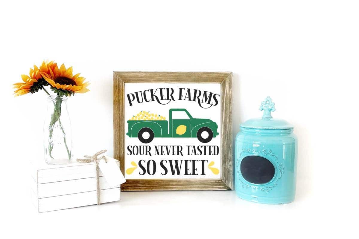 Horizontal image of a farmhouse sign with Pucker Farms lemon truck and text which reads sour never tasted so sweet with simple decor.