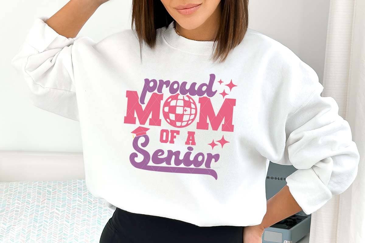 Horizontal image of a mom in white sweatshirt which reads proud mom of a senior with a disco ball SVG Cricut design in heat transfer pink and purple vinyl.