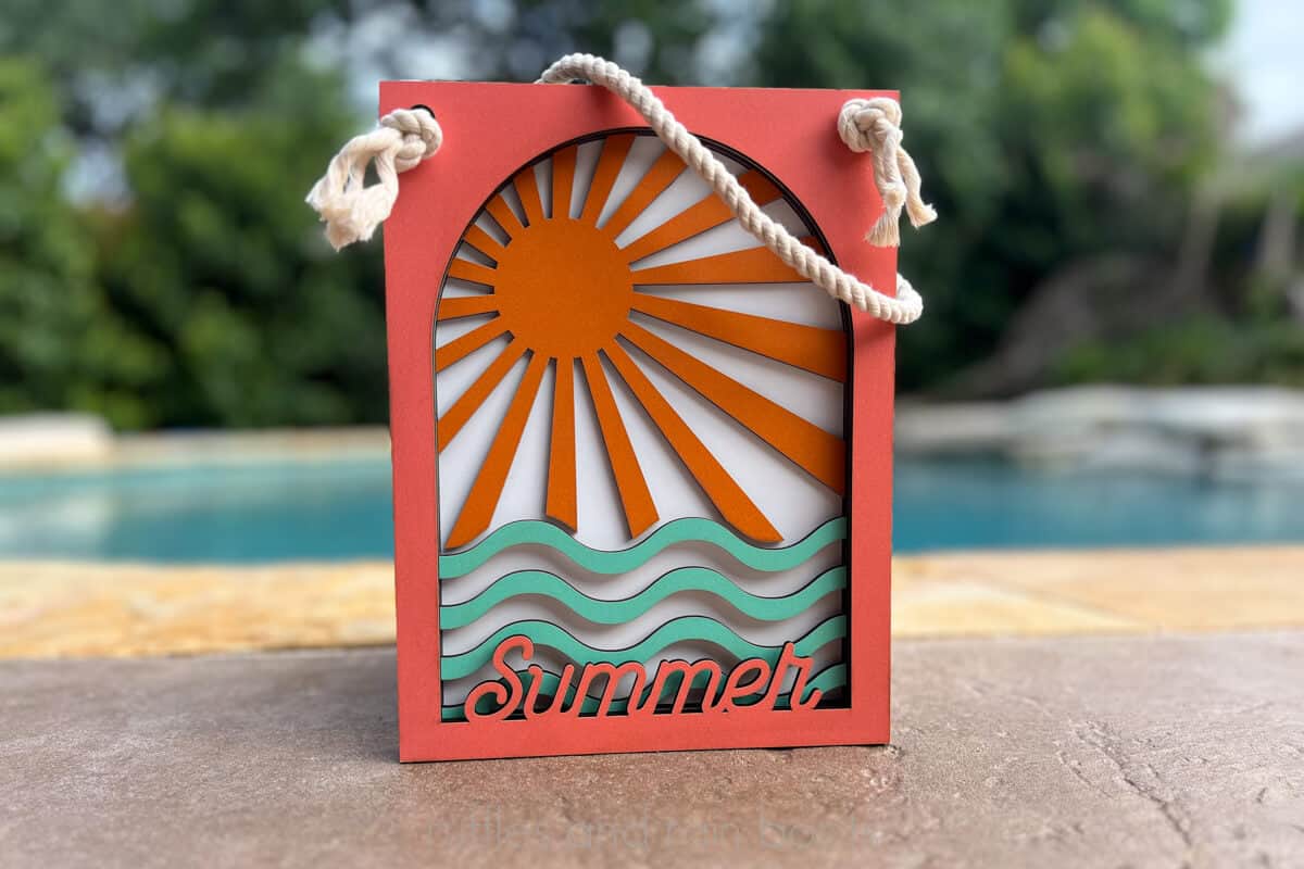 Horizontal image of a multi-layer summer door sign with a rope hanger in colored MDF placed in front of a pool.