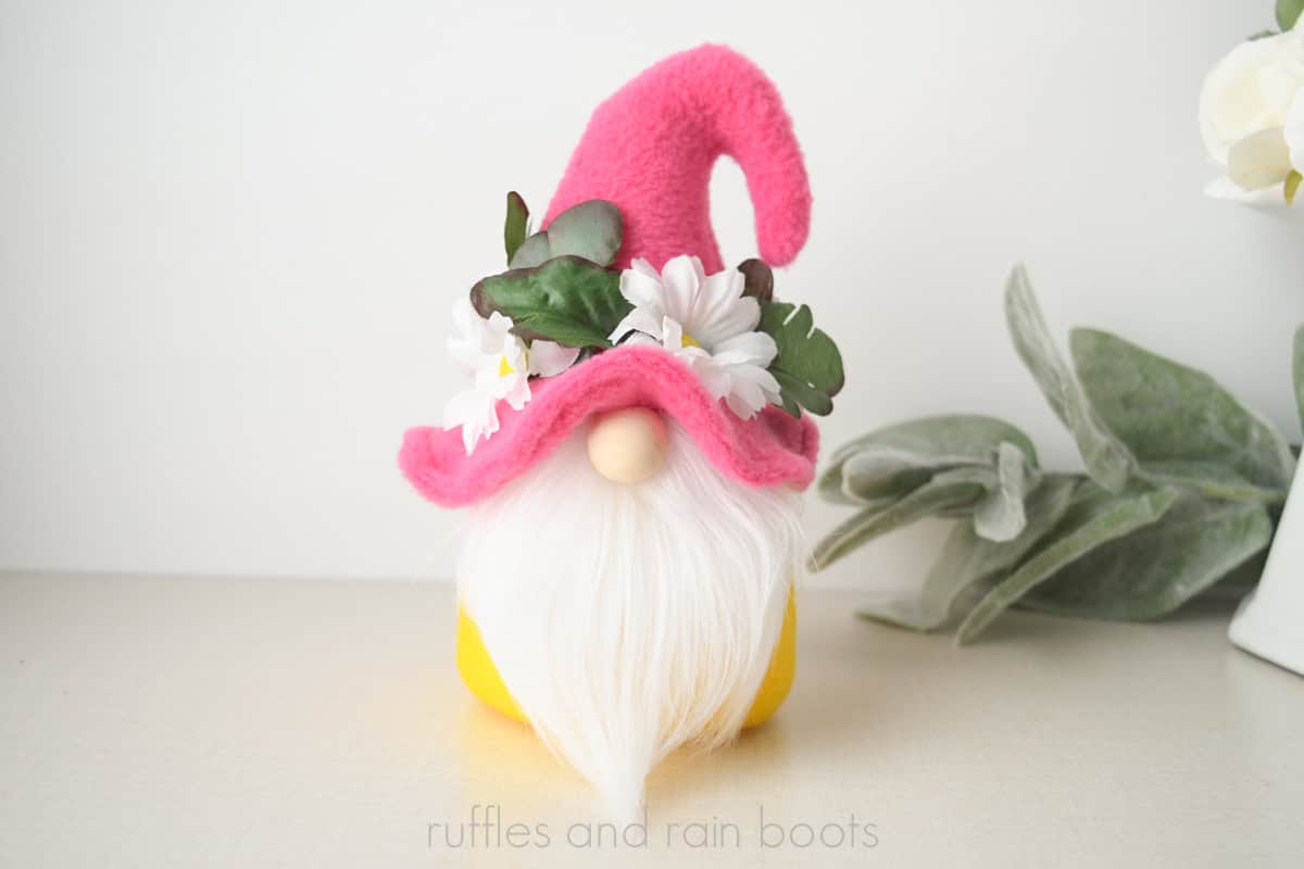 Horizontal image of a hooked hat summer gnome with a floral brim, pink hat, yellow body, and white beard.