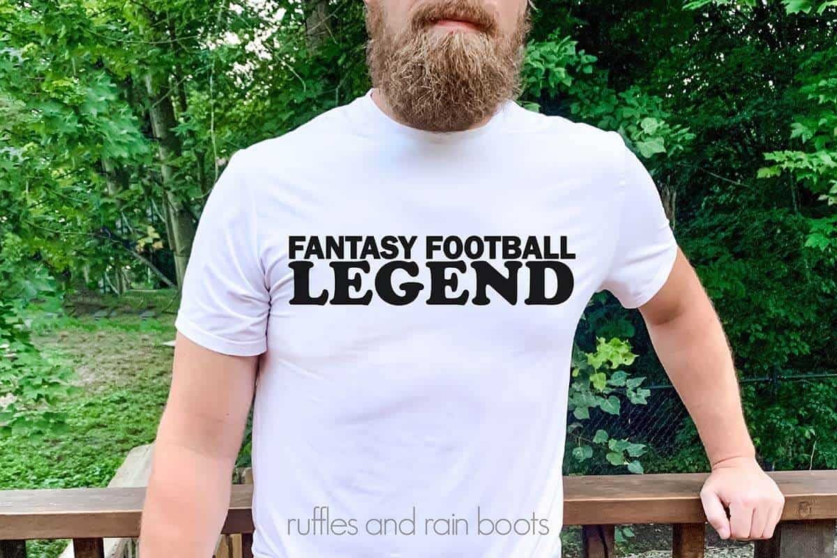 Horizontal image of a bearded man on a porch in a forest wearing a white t-shirt which reads fantasy football legend.
