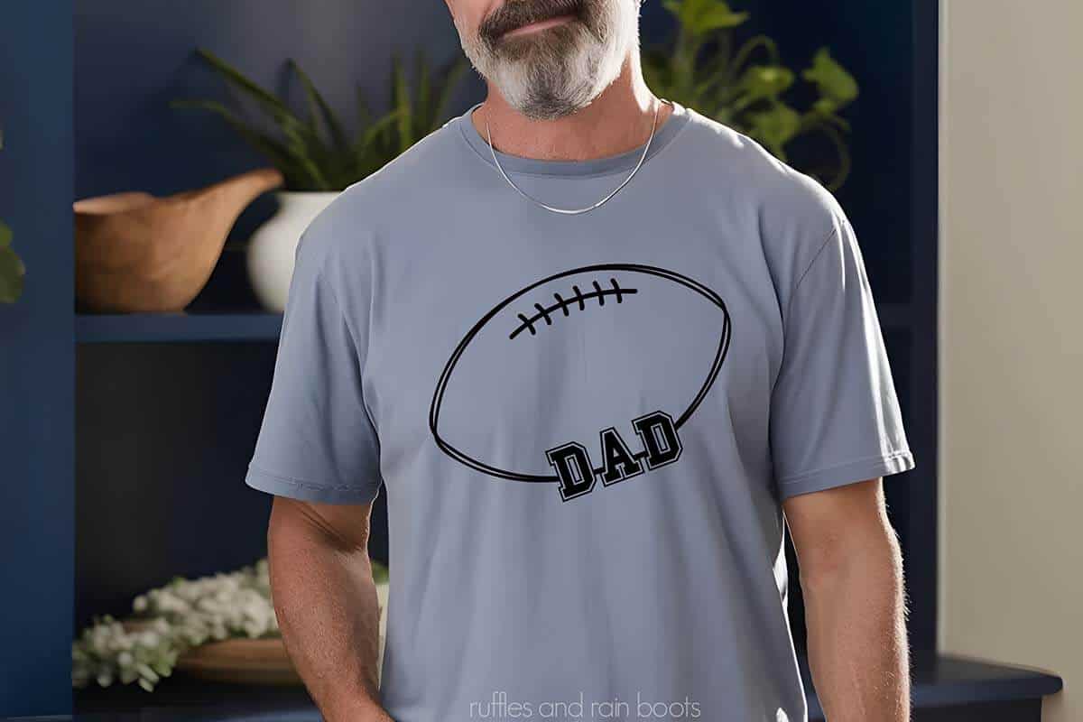 Horizontal image of an older bearded man standing in front of a bookshelf wearing a light blue shirt with a hand drawn football with Dad in varsity style lettering.