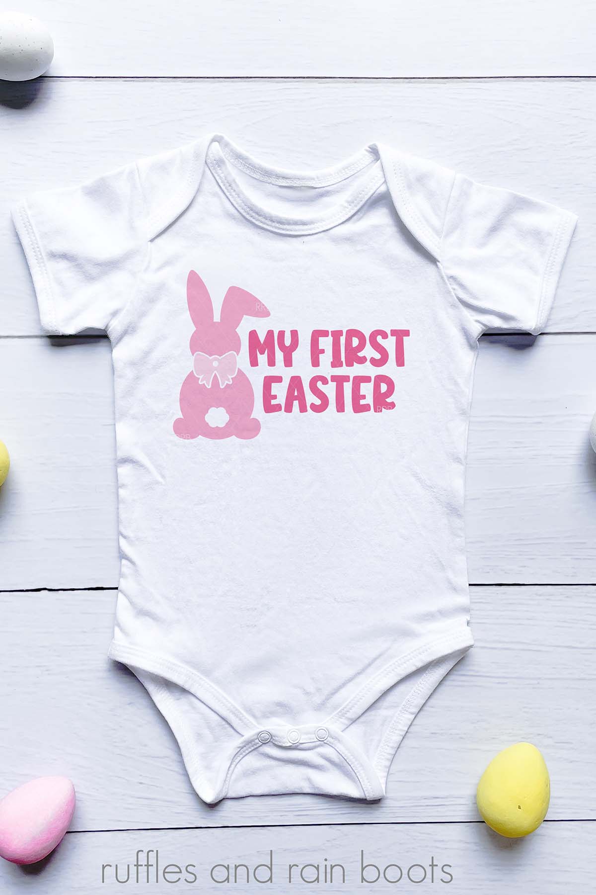 Vertical image of a white baby body suit with a pink bunny with a bow svg and my first Easter in pink.