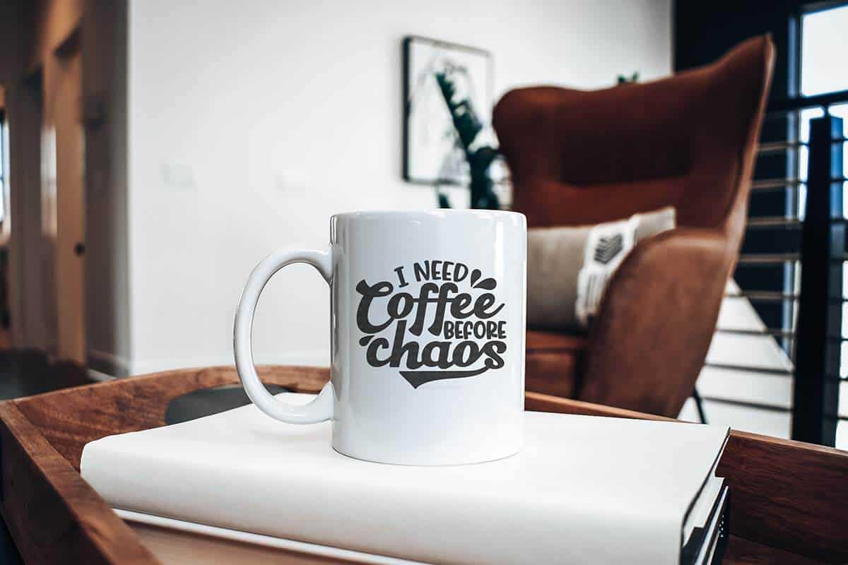 Horizontal image of a stylish room with a white ceramic mug with the words I need coffee before chaos in black vinyl.