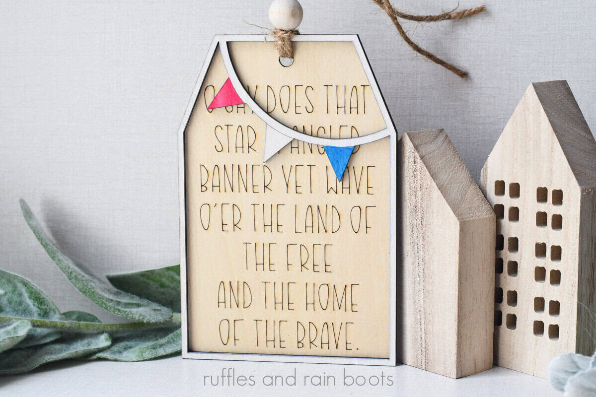 Horizontal image of a scored wood tag with a frame and a penant in red, white, and blue for Independence Day decor.