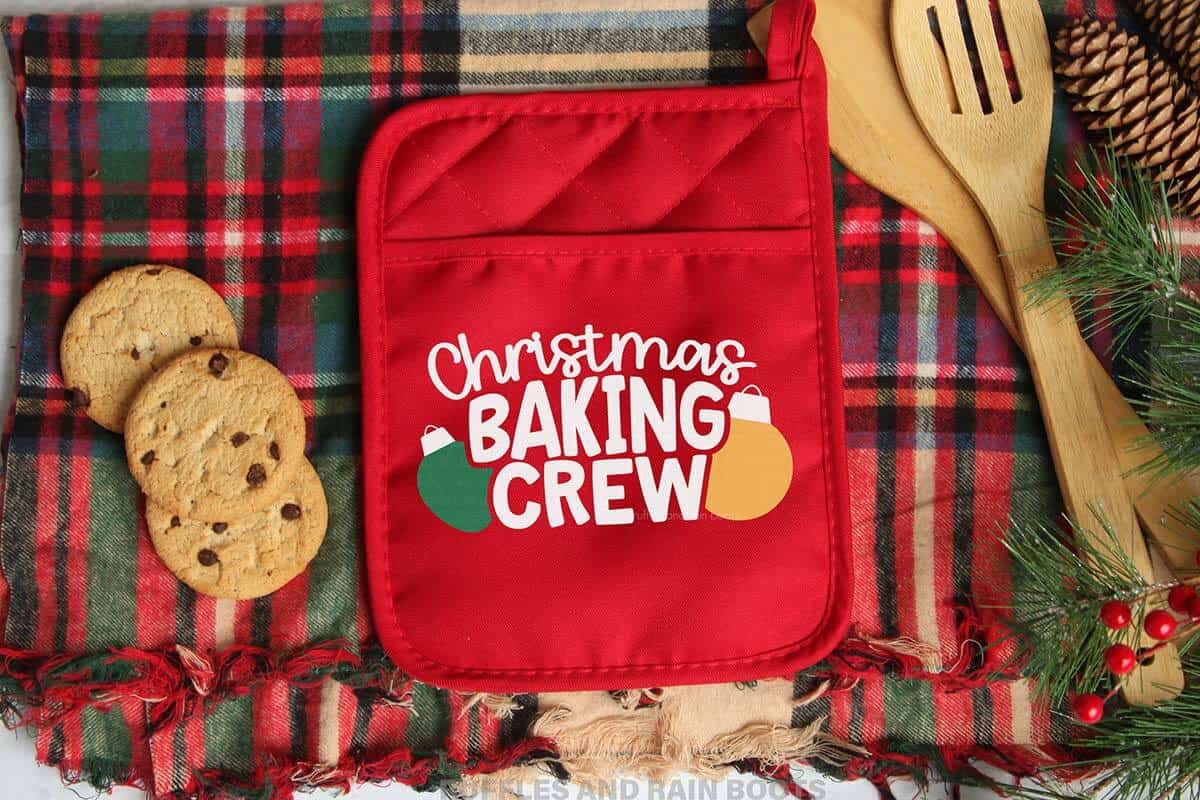 Horizontal image of a red pot holder on a plaid towel with a fun and playful Christmas baking crew SVG with ornaments frame from Ruffles and Rain Boots SVG.