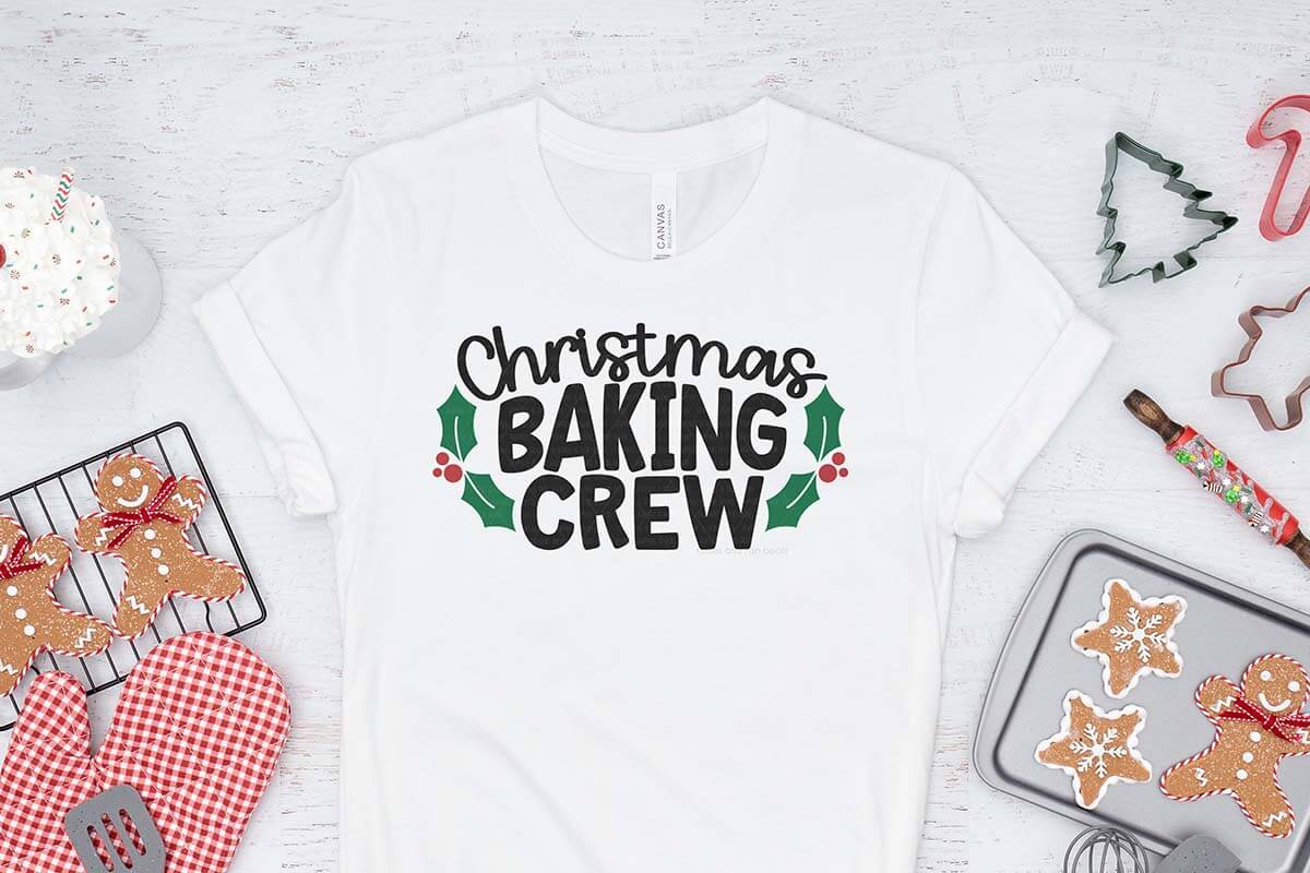 Horizontal image of a white t-shirt on a white table with vinyl which reads Christmas baking crew and holly and berries SVG.