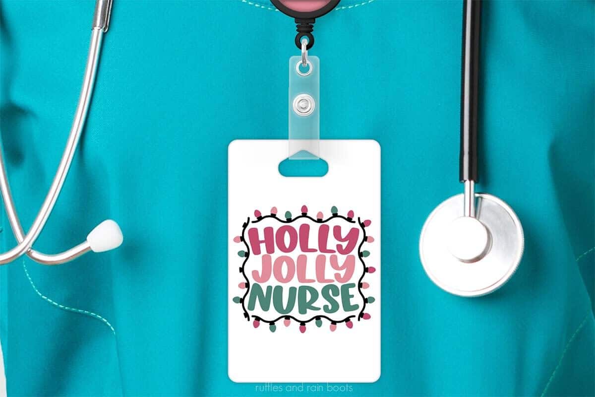 Horizontal image of badge reel hanging on scrubs with a white card hanging from it which reads holly jolly nurse surrounded in a frame of Christmas lights.