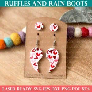 Square, close up image of a set of laser cut acrylic earring studs, shaped earrings, and a jewelry card from Ruffles and Rain Boots SVG.
