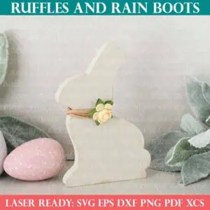 Square close up image of a white bunny shelf sitter with antique accents next to greenery and painted, speckled Easter eggs.